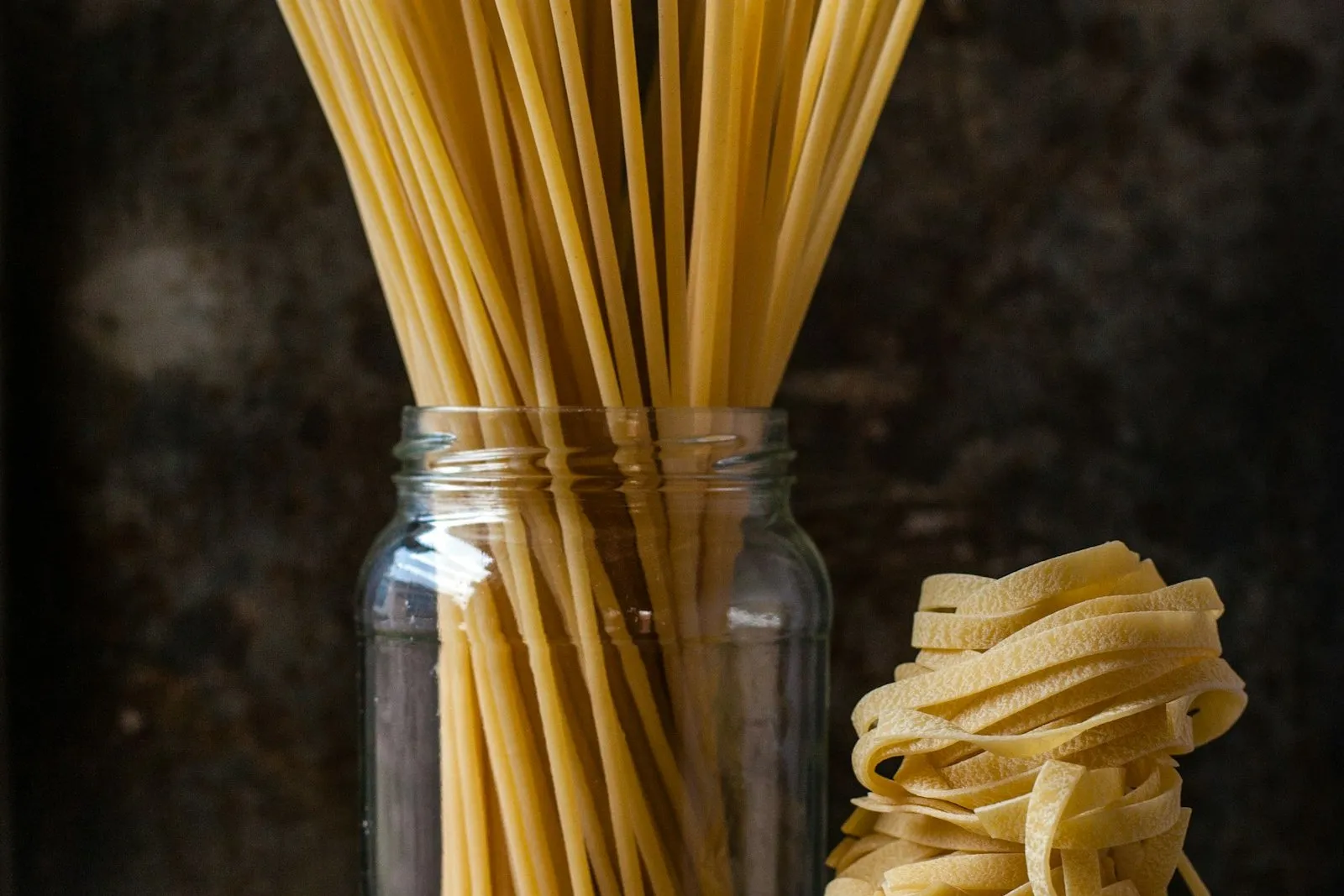 Suchy makaron spaghetti w szklanym słoiku i gniazdo makaronu wstążki